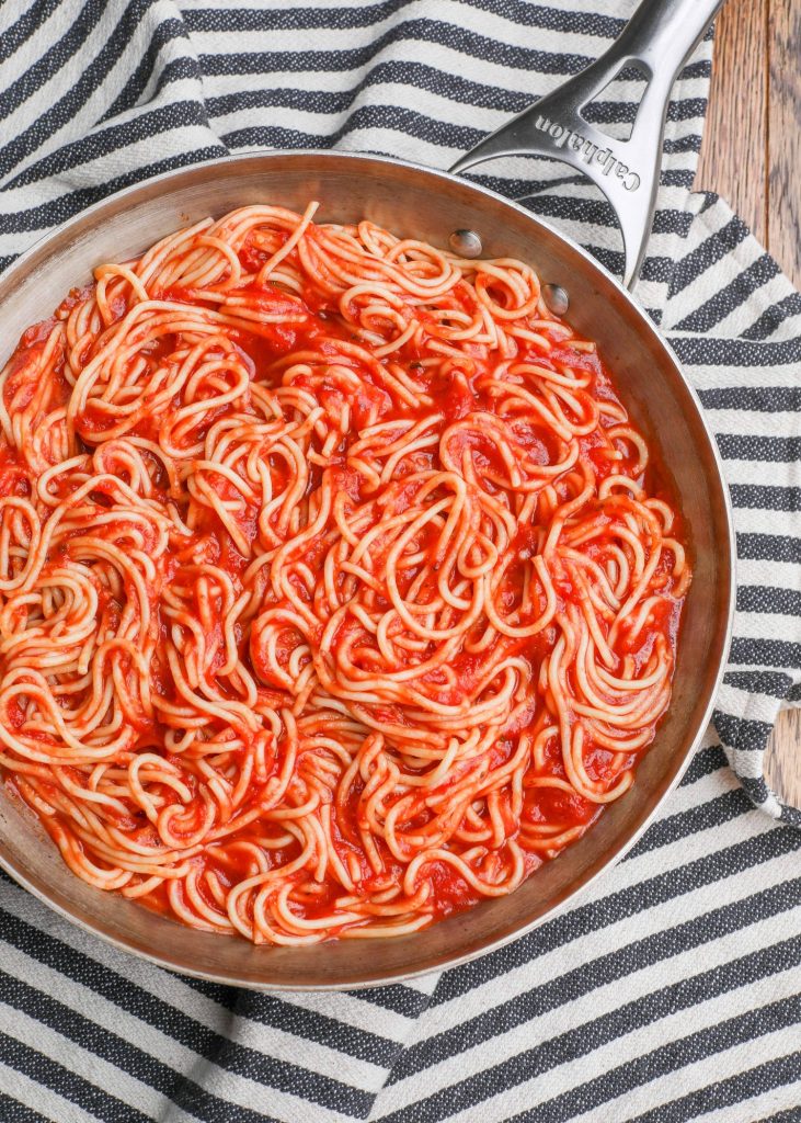 spaghetti noodles with sauce in pan with black and white towel