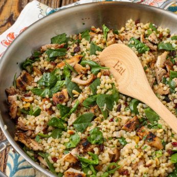 spinach and israeli couscous in large skillet with wooden spoon