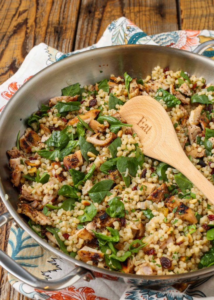 spinach and israeli couscous in large skillet with wooden spoon