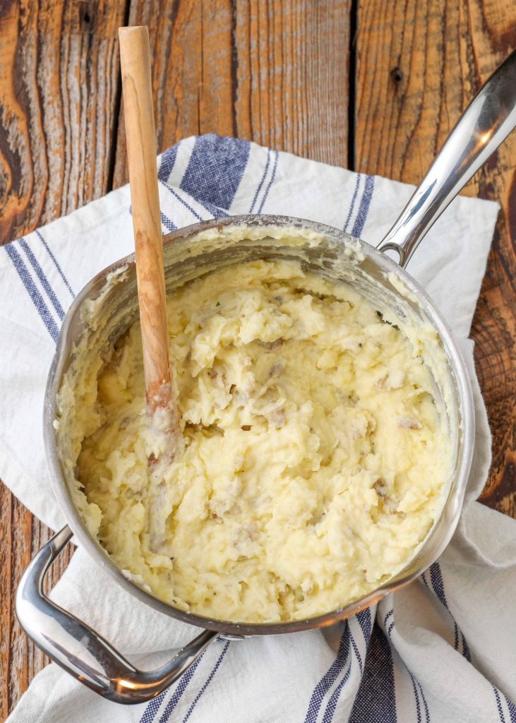 creamy rich mashed potatoes in pot with wooden spoon