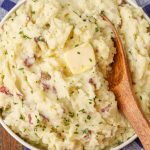 mashed red potatoes with butter in round dish with wooden spoon