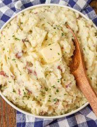 mashed red potatoes with butter in round dish with wooden spoon
