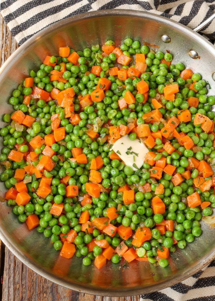 carrots and peas in pan with butter and striped towel
