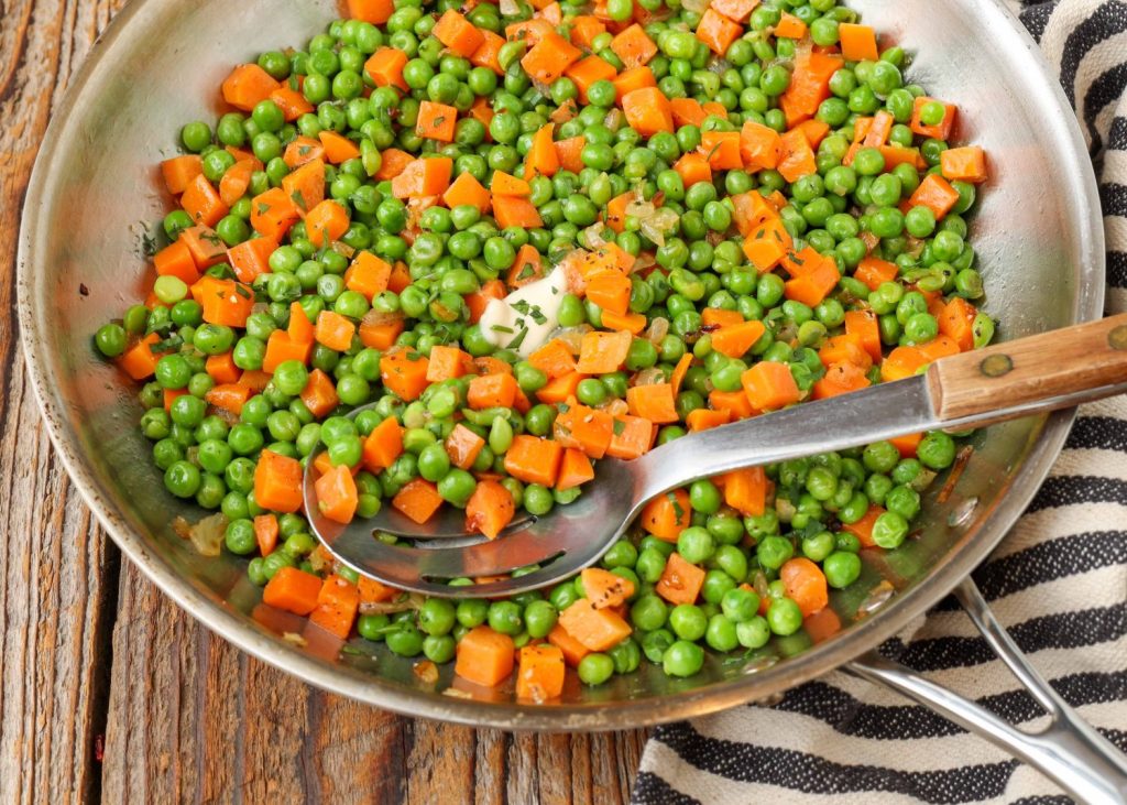 peas and carrots in stainless pan with serving spoon