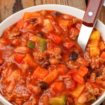 chili with bell peppers in bowl with wooden spoon