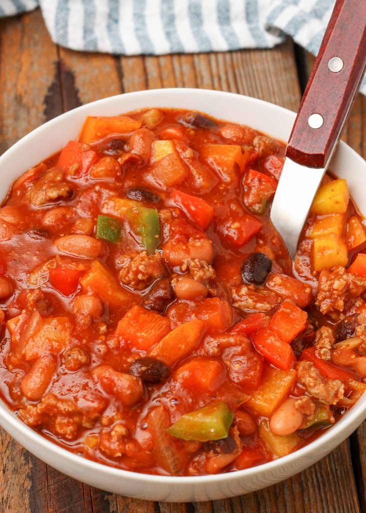 chili with bell peppers in bowl with wooden spoon