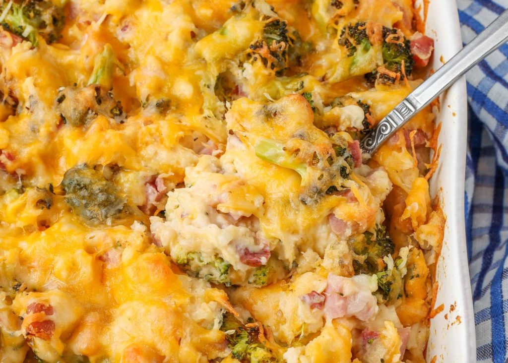 cheesy potato casserole with broccoli and ham in white dish with serving spoon