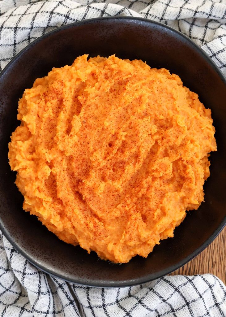 mashed sweet potatoes in black bowl with plaid towel