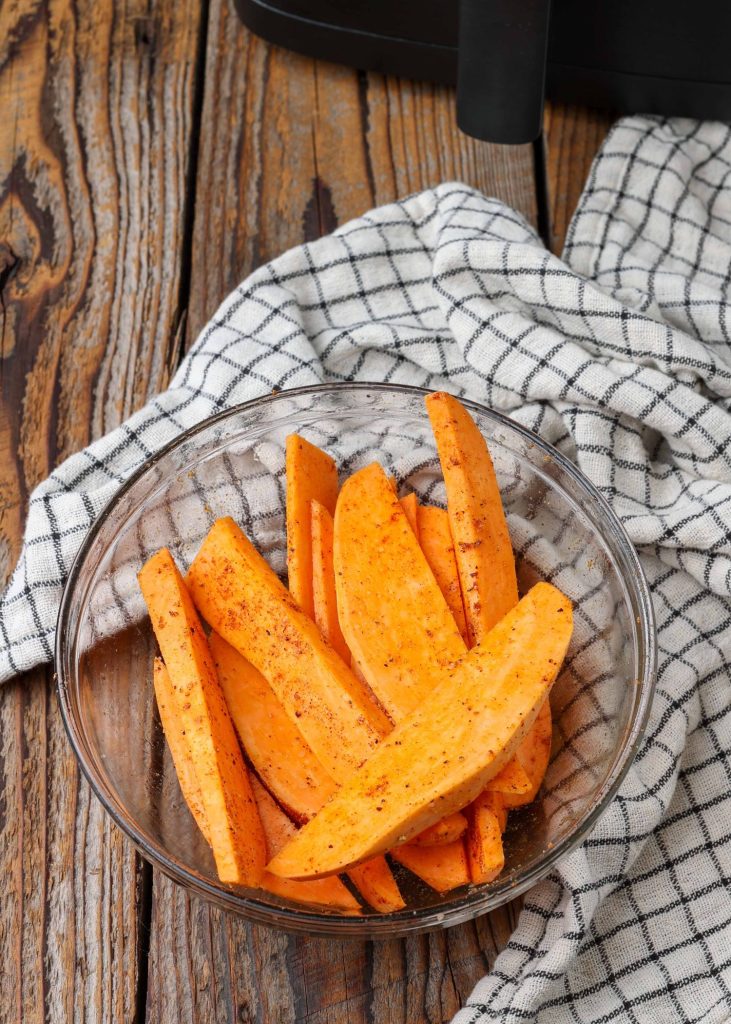 Air Fryer Sweet Potato Wedges seasoned in glass bowl with blue and white towel