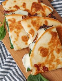 Spinach Quesadilla with fresh spinach and melted cheese on cutting board with blue and white towel