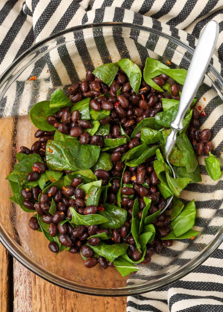 spicy black beans with spinach in glass bowl