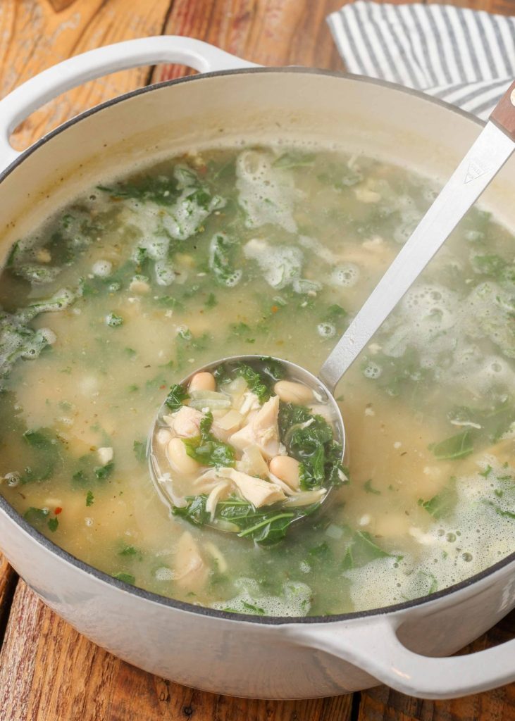 white bean, kale, and chicken soup in white pot with ladle