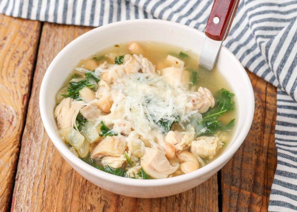 chicken soup with kale and white beans in white bowl with wooden spoon