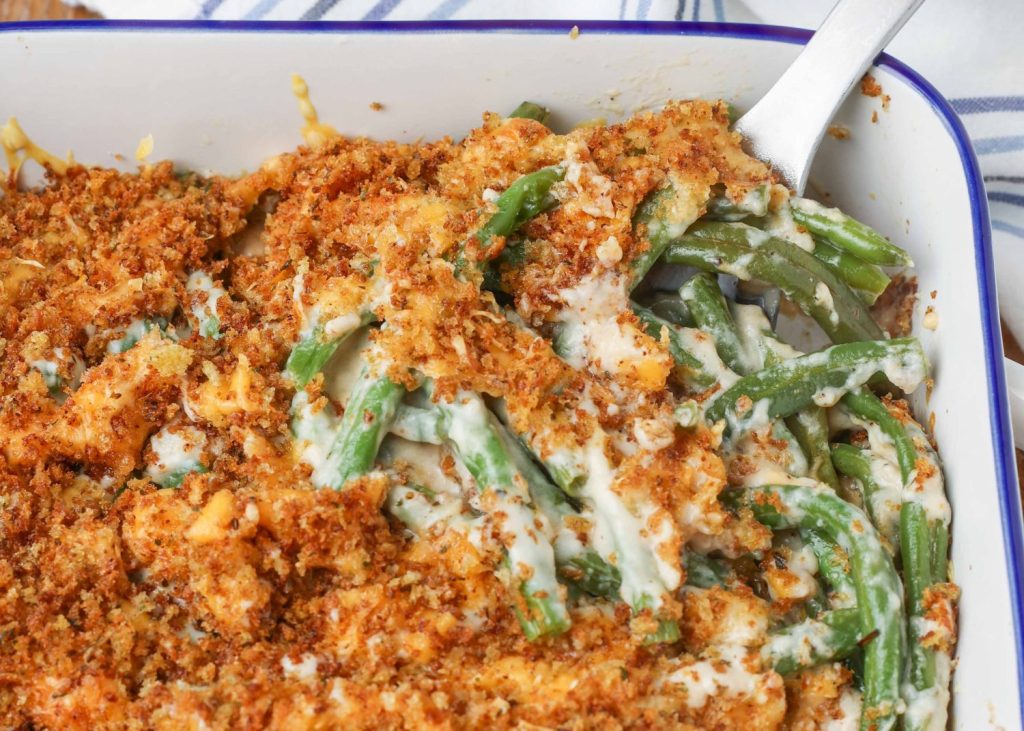 green beans in cream sauce with crispy bread crumb topping in a white baking dish with spoon