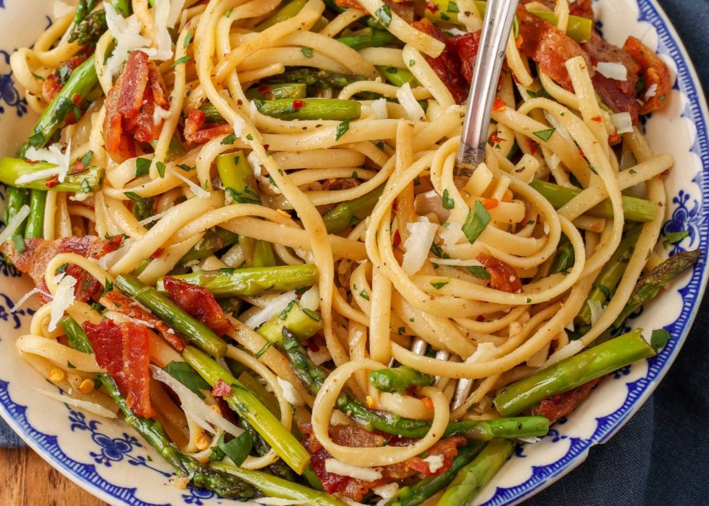pasta with asparagus and bacon in blue and white bowl with fork