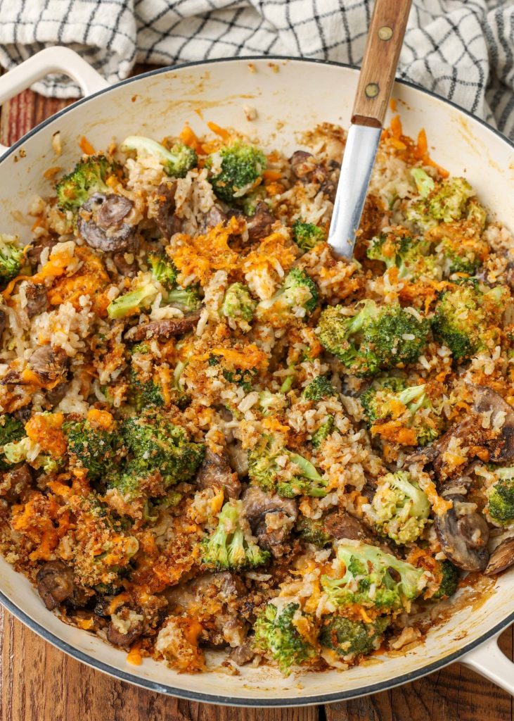broccoli, mushrooms, rice with buttery topping and wooden handle spoon in casserole skillet