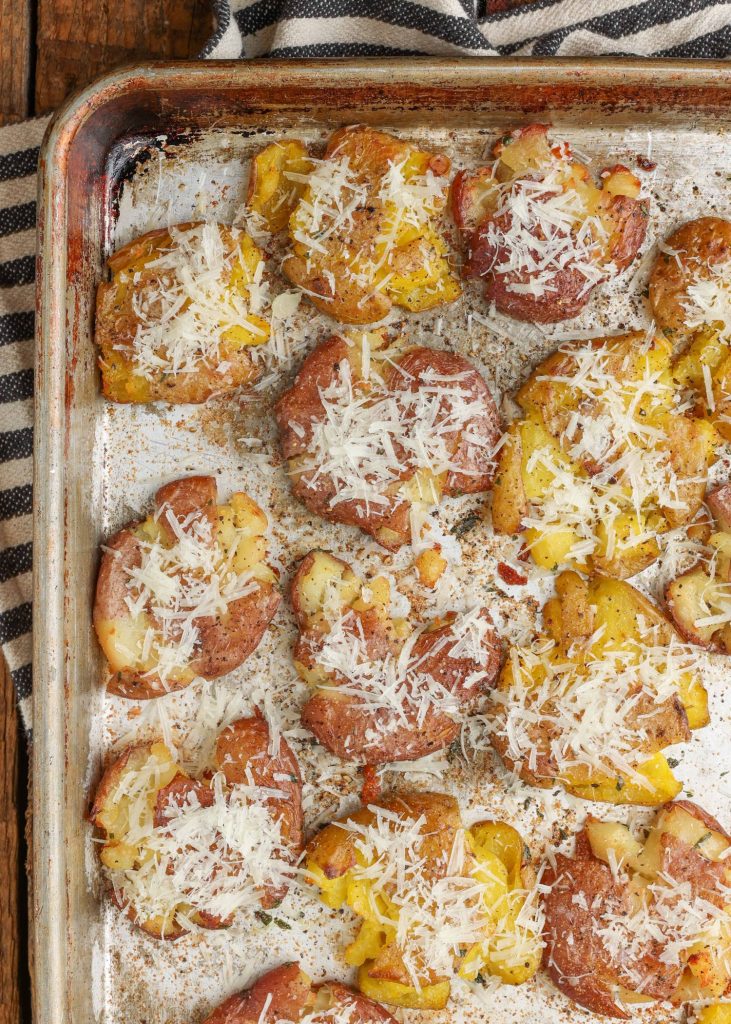 smashed potatoes have been pressed down onto a greased metal baking sheet in this image, sprinkled with shredded cheese and spices