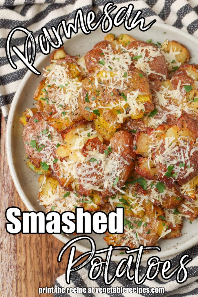 a top down photo of parmesan smashed potatoes on a white plate, covered in freshly shredded parmesan cheese and parsley flakes. white lettering has been overlaid the image to read: "garlic parmesan smashed potatoes"
