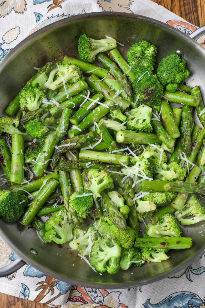 sauteed broccoli with asparagus topped with parmesan in stainless pan