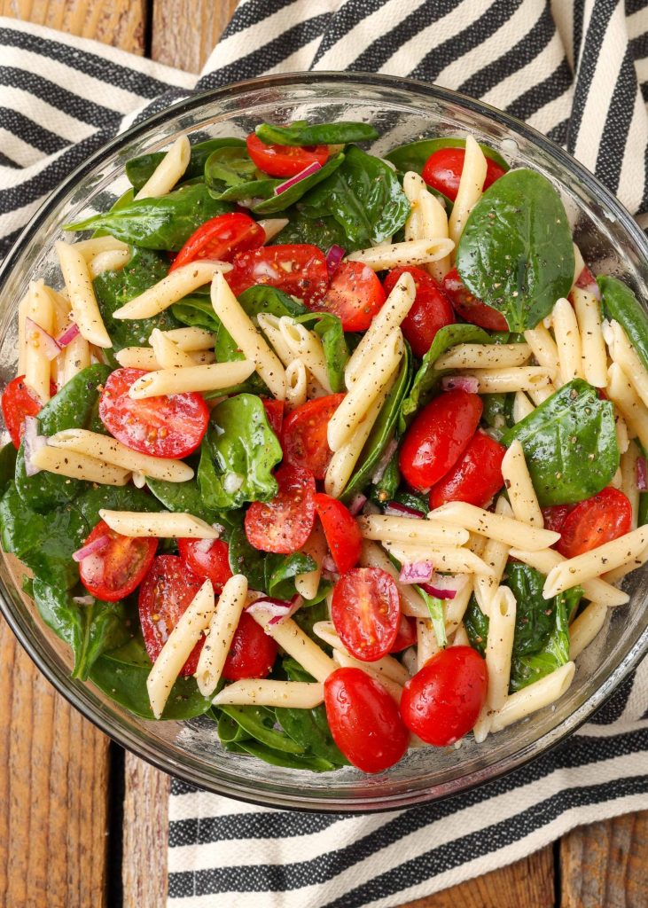 cold pasta salad with tomatoes in clear mixing bowl 