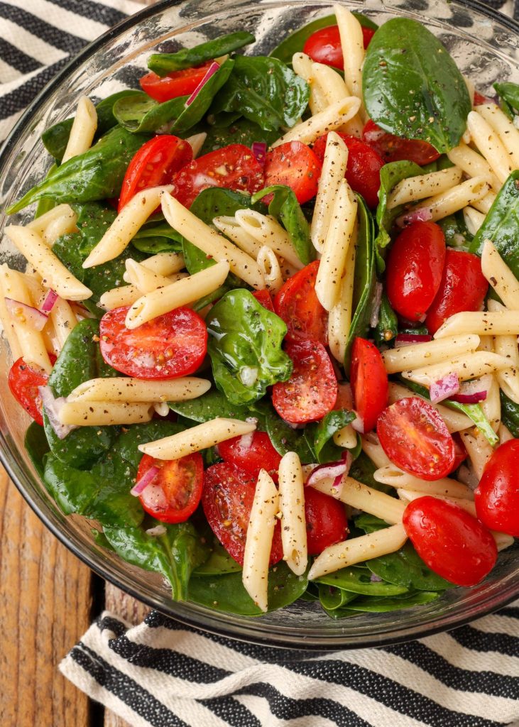 spinach tomato pasta in bowl with black and white towel