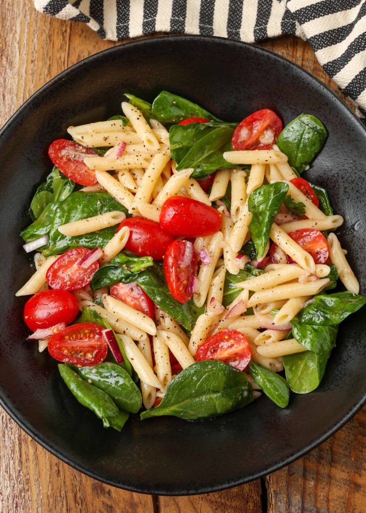 tomato spinach pasta salad in black bowl with striped napkin