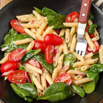 black bowl and wooden spoon holding spinach pasta salad
