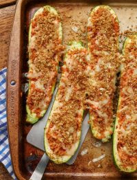 a spatula is visible scooping up a finished zucchini boat from the sheet pan, ready to eat