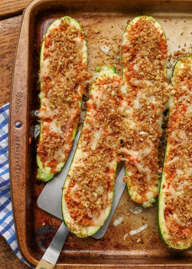 a spatula is visible scooping up a finished zucchini boat from the sheet pan, ready to eat