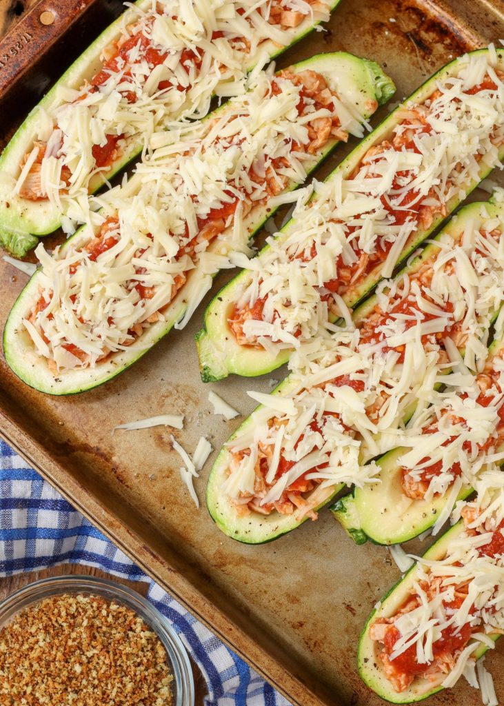 mozzarella cheese has been sprinkled on top of zucchini boats lying side by side in a sheet pan, ready for bread crumbs to be added