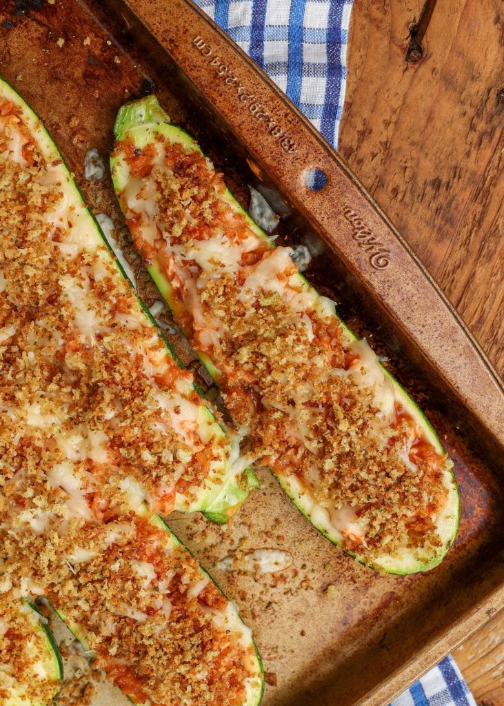 a top down shot of the corner of a copper sheet pan with zucchini boats fresh from the oven, topped with mozzarella and bread crumbs