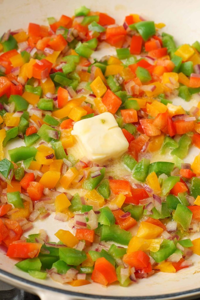 a pat of better is slowly melting in this pan full of colorful pieces of peppers and onions