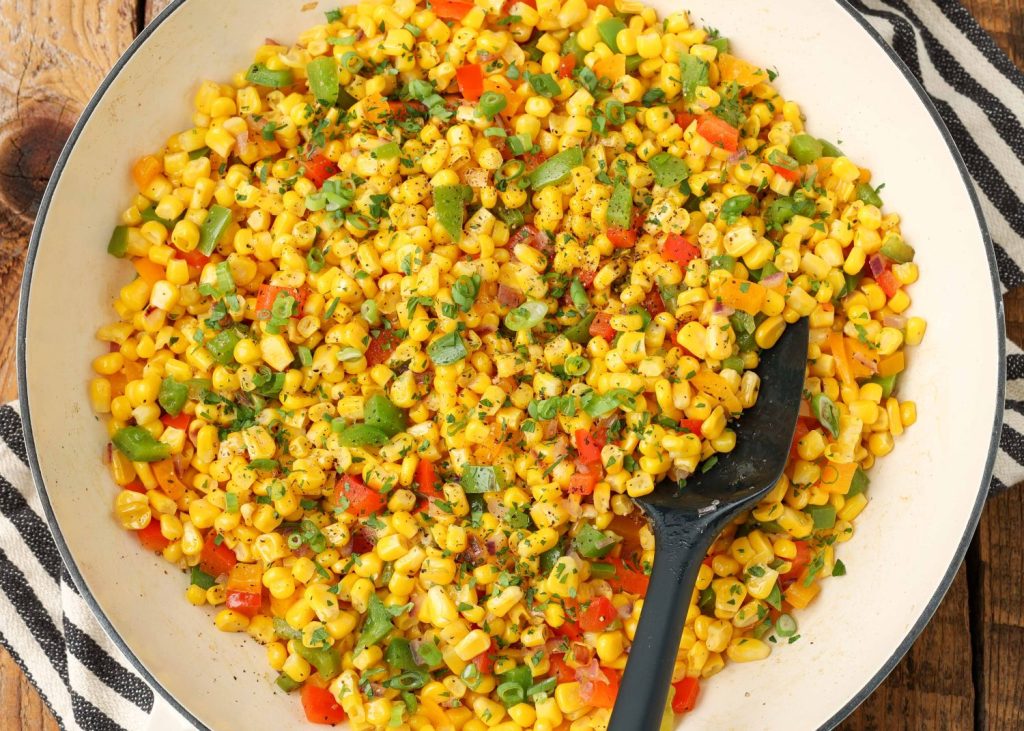 colorful pieces of peppers, red onion, and corn kernels fill this shallow white bowl with a dark rim