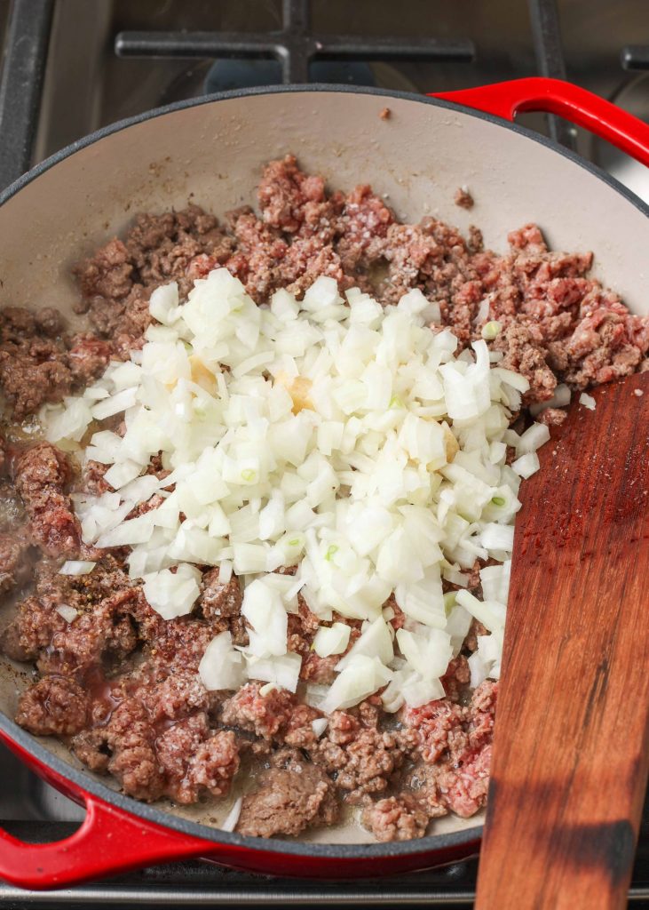 chopped onions and garlic have been piled atop cooked ground beef in a skillet