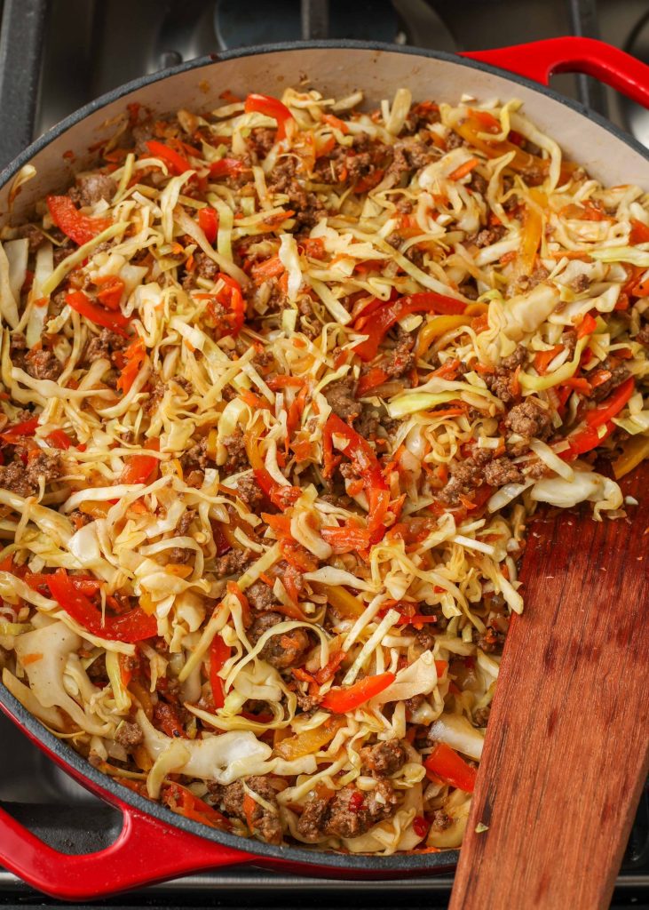 finished and ready to serve, this ground beef and cabbage dish fills the red skillet with a wooden spatula sticking out