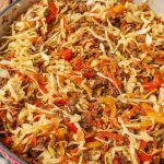 a close up photo of ground beef, cabbage, carrots, and bell peppers with onions and garlic in the skillet