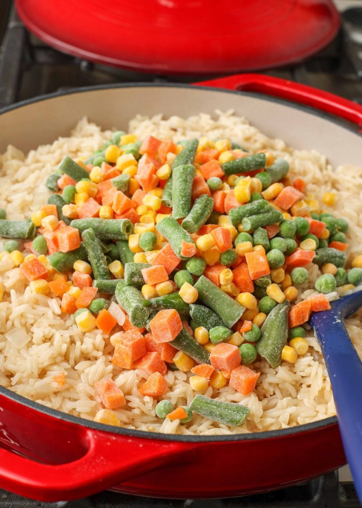 frozen vegetables are piled atop freshly cooked rice in a skillet