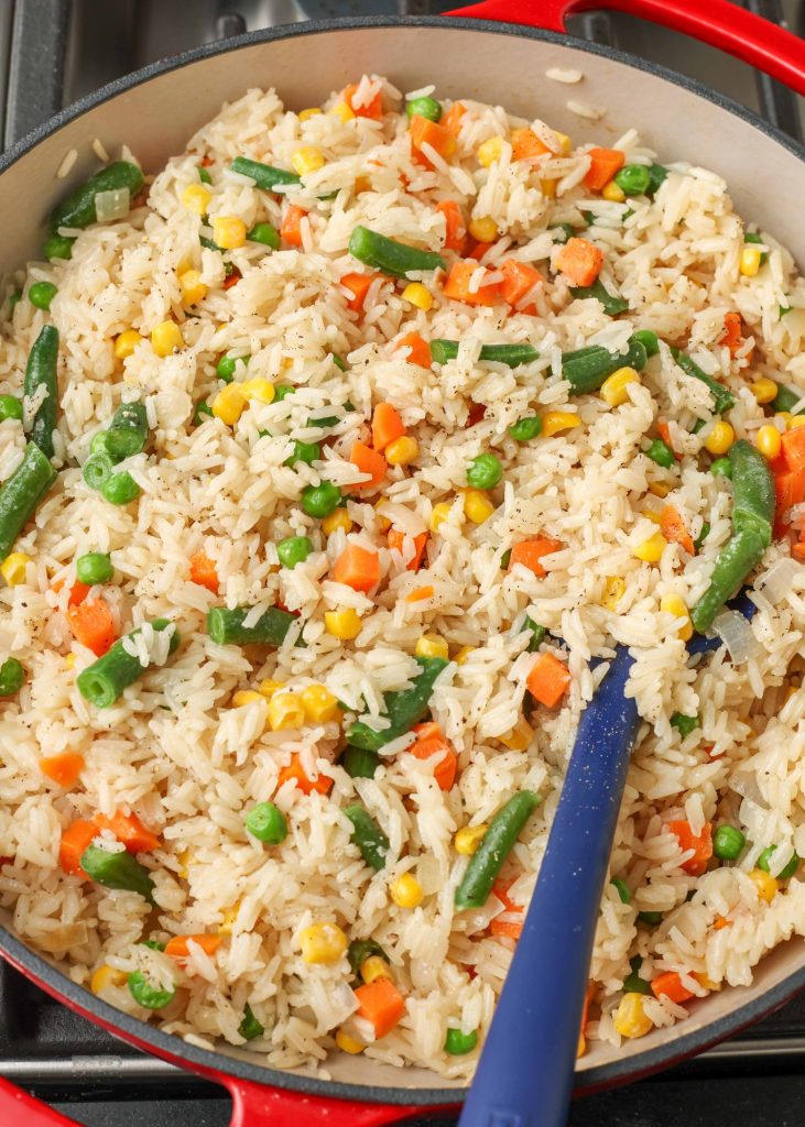 fully cooked mixed vegetable rice rests in the skillet, with a long blue spatula
