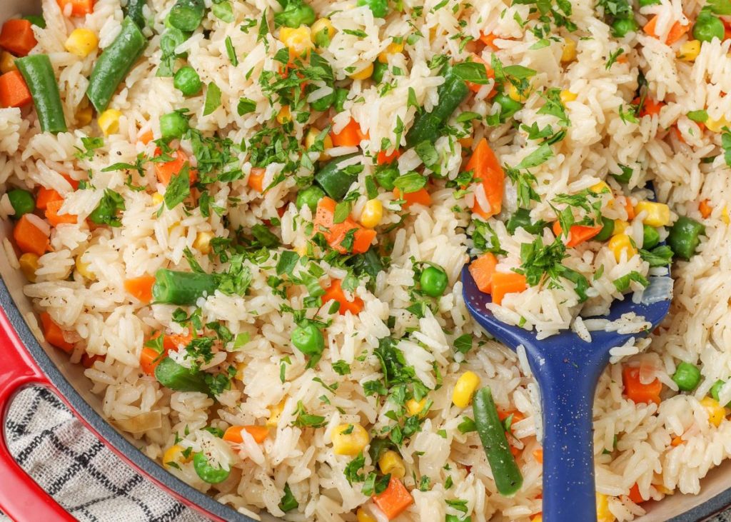 fully cooked rice with vegetables rests in the skillet, with a long blue spatula