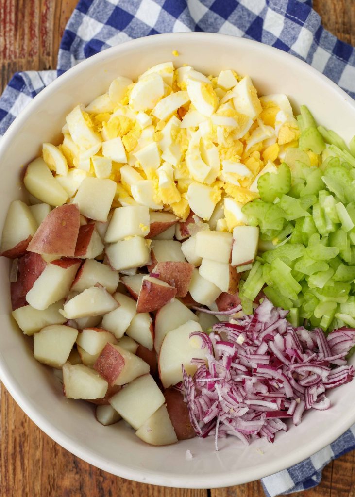 A bowl contains all of the ingredients for a potato salad except for the sauce, arranged by color