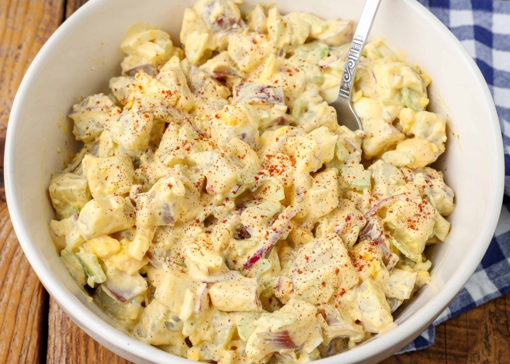 A bowl of potato salad with red onions and celery, sprinkled with paprika