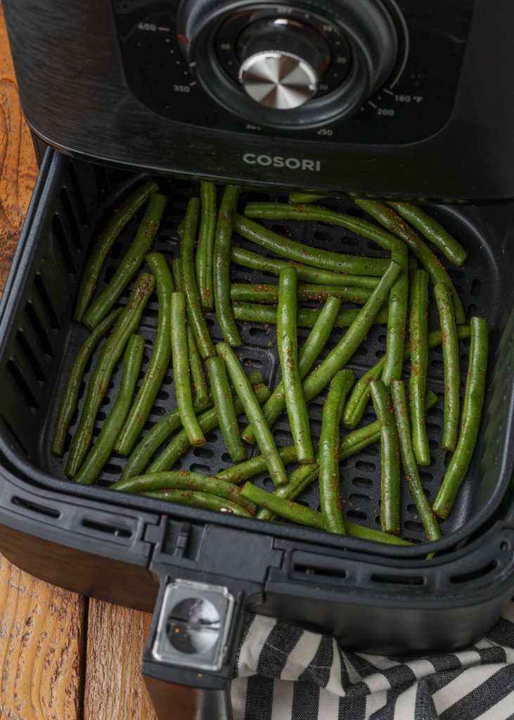 an image of an open cosori air fryer with seasoned green beans, ready to fry