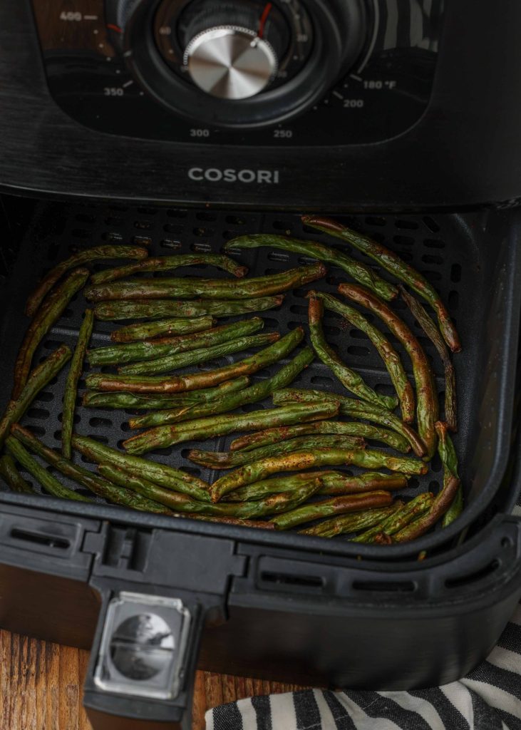 fried green beans are pictured within the open basket of this cosori air fryer
