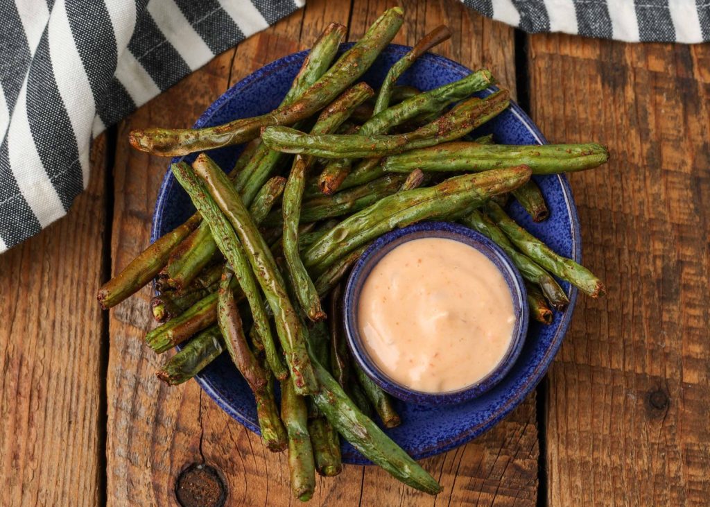 a plate of air fryer green beans is ready to be eaten, served with bang bang sauce