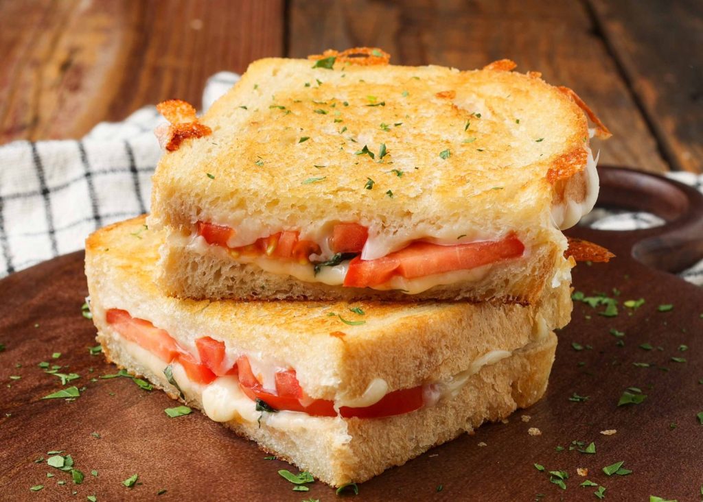 two halves of a Caprese Grilled Cheese have been stacked one atop the other on a dark wooden serving tray with a black and white  stripped napkin visible in the background