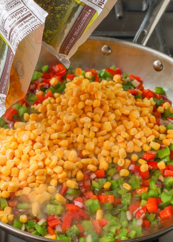 an image of frozen corn being poured into a skillet with bell peppers and onions