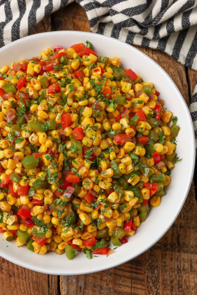 a top down shot of a white bowl filled with fiesta corn and topped with cilantro