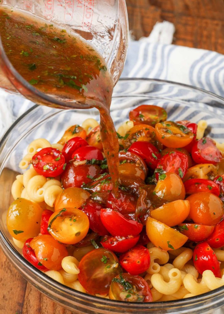 pouring the marinade over the tomatoes and pasta in this image
