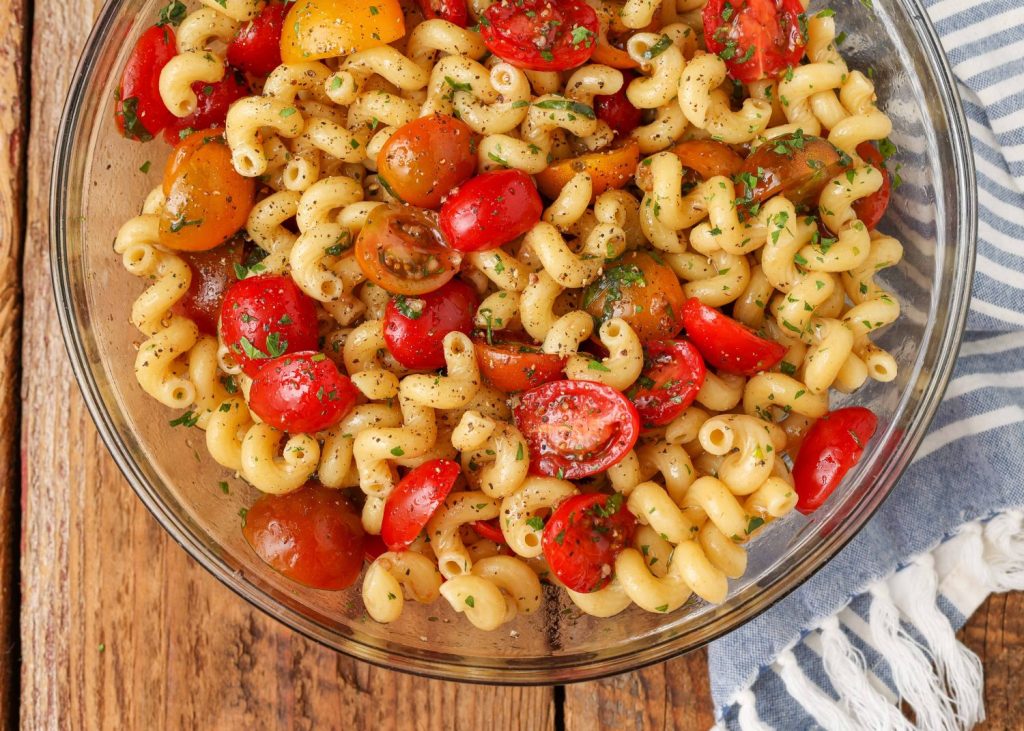a clear glass bowl full of balsamic marinated tomatoes and cavatappi pasta