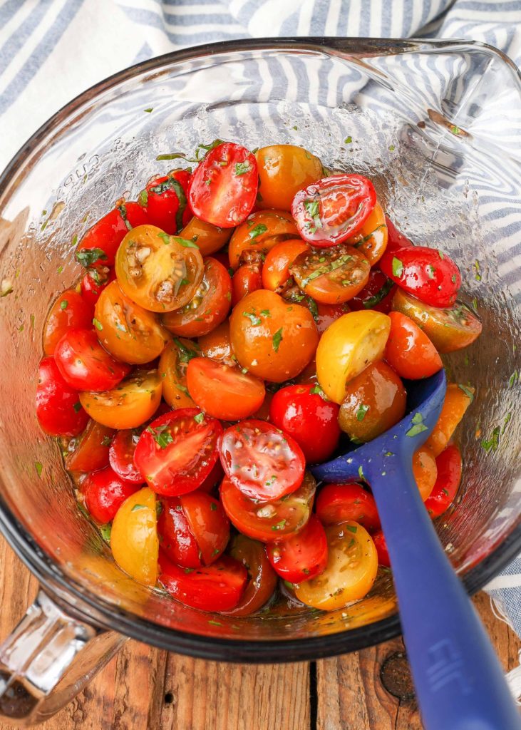 the tomatoes have been stirred with a blue spatula in a clear glass bowl